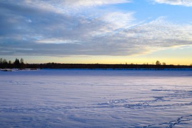 Donmuş nehrin üzerinde kış günbatımı. Karda insan ayak izleri görülebilir..
