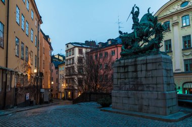 Kopmantorget Meydanı 'nın geniş açısında tarihi binalar ve alacakaranlıktaki Aziz George ve Ejderha heykeli, Stockholm, İsveç