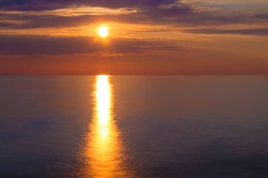 Long exposure view of the setting sun between clouds over the sea