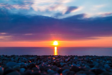 Long exposure view of the pebble beach on the background of the setting sun over the sea