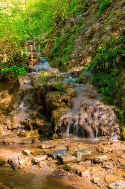 Waterfall and wooden stairs in the park Berendeyevo Tsarstvo in sunny summer day, Sochi, Russia