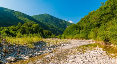 Panoramic view of Makopse river flowing in ravine on the background of Tamyurdepe mountain in the light of the setting sun, Sochi, Russia
