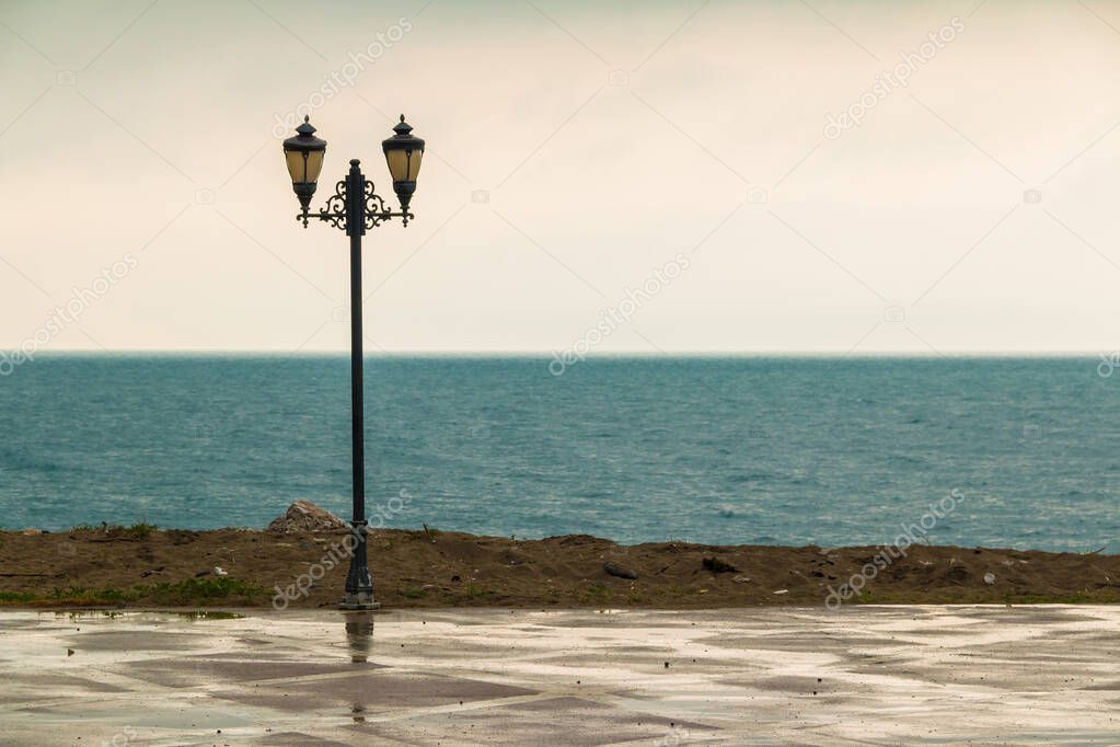 The lamppost standing on the embankment on the background of sea in rainy day