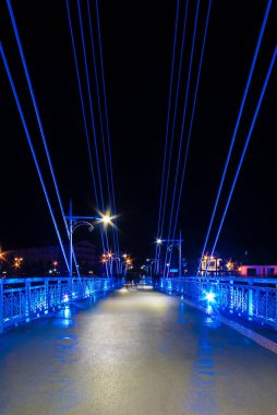 Perspective view of illuminated span of the Bridge of Lovers with people blurred in motion at night, Tyumen, Russia
