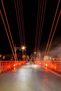 Perspective view of illuminated span of the Bridge of Lovers with people blurred in motion at night, Tyumen, Russia