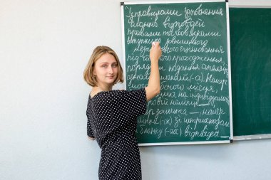  Ofisteki yeşil kuruldaki kız öğrenci tebeşirle bir görev yazıyor.