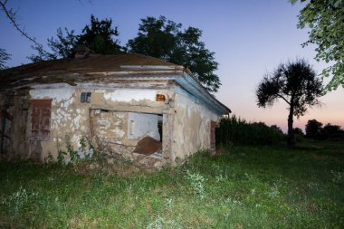 Eski bir demir çatının altındaki duvarlarında delikler olan eski bir köydeki harabe kerpiç evi.      