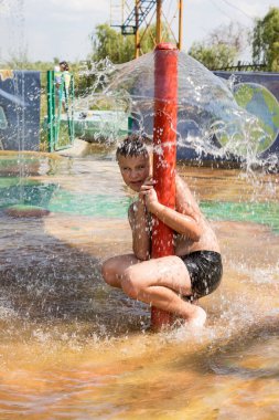 Su parkında bir çocuk çeşmenin altında oturuyor.