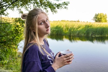 Bir kız orman gölünün kıyısında çay ya da kahve içer.