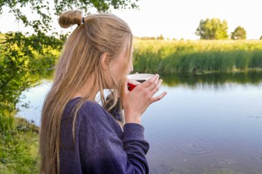 Bir kız orman gölünün kıyısında çay ya da kahve içer.