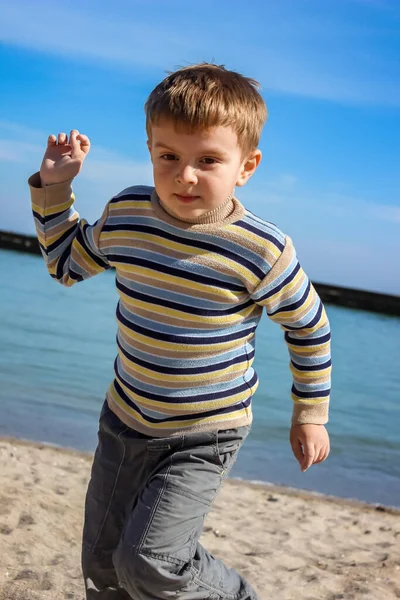 Çizgili balıkçı yakalı bir çocuk deniz kıyısı, sahil, bahar boyunca koşar.