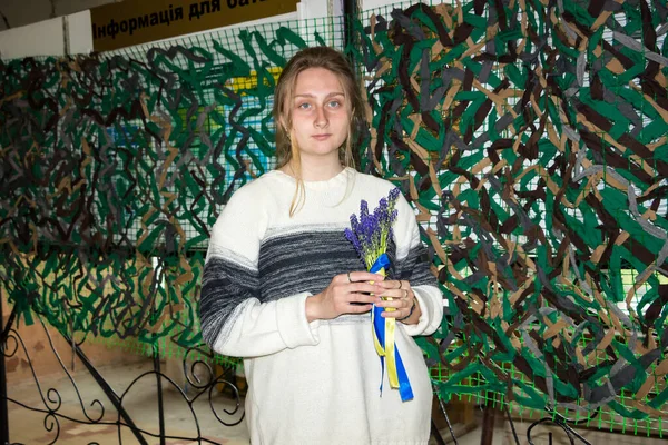 春の青い花を持つ若い女の子黄色のリボンは 軍事迷彩ネット ウクライナの背景に手を保持しています — ストック写真