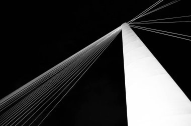 Beyaz yüksek metal bir kolon şeklinde soyutlama yukarı çıkıyor ve beyaz ipler bu sütundan siyah arka planda ışınlar halinde çıkıyor.