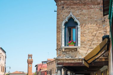 Eski bir tuğladan evin köşesinde mavi gökyüzüne ve eski şehrin bir kısmına çiçek açmış antik bir pencere.