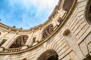 Bottom up view of a part of an old rounded stone building and blue sky with clouds