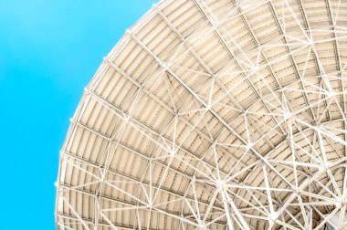 Bir radyo teleskopunun yuvarlak yüzeyinin mavi gökyüzüne karşı birçok metal destekli alt görüntüsü