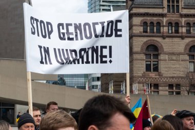 Toronto, ON, Kanada 10 Nisan 2022: Ukraynalıların soykırımını durdurmak için düzenlenen Ukrayna Kanada Kongresi mitinginde Ukrayna şehir merkezindeki Nathan Phillips Meydanı 'nda pankart ve bayraklı protestocular. Putin ve Rus ordusu Uk 'u yok etmek istiyor.