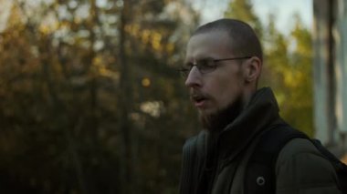 Gözlüklü sakallı bir adam elektronik sigara içiyor ve eğleniyor. Dışarıda duran sırt çantalı bir vapurcu kafayı bulmuş gibi görünüyor. Bulanık ağaçlar arka plan