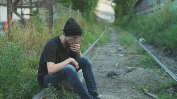 ホームレスの男の喫煙タバコは 鉄道の上に座って 煙が吹く 貧困や惨事に巻き込まれ解雇され解雇され焼かれました 社会問題失業概念 — ストック動画