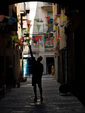 Sokakları süsleyen küçük renkli bayraklarla Barselona caddesi. Arka planda duran biri bayraklara tek eliyle dokunmaya çalışıyor.