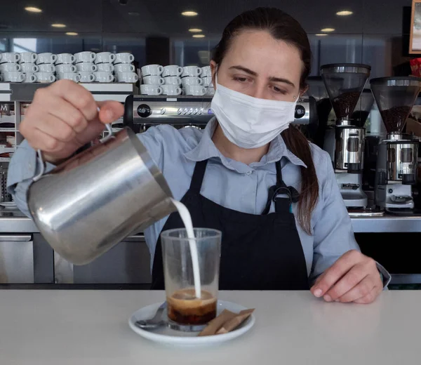 waitress behind the bar pouring milk from a metal jug into a coffee cup