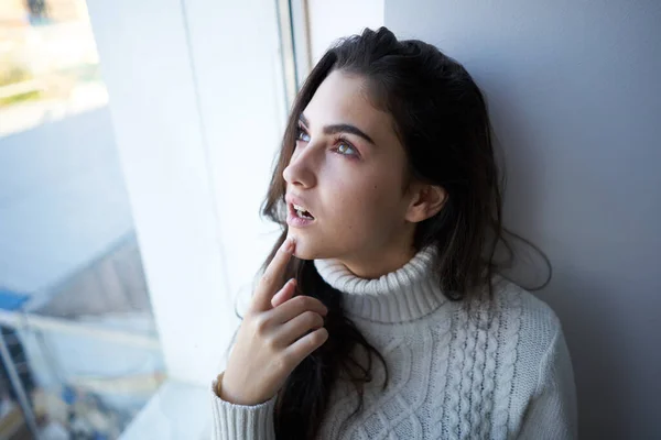 Morena en un suéter blanco mira por la ventana depresión — Foto de Stock