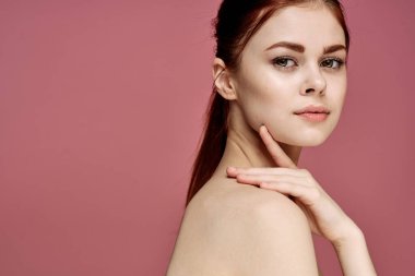 Çıplak omuzlu, çekici, pembe arka planı olan bir kadın.