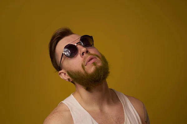 Un homme barbu avec une expression sérieuse dans un t-shirt blanc avec des tatouages sur les bras — Photo