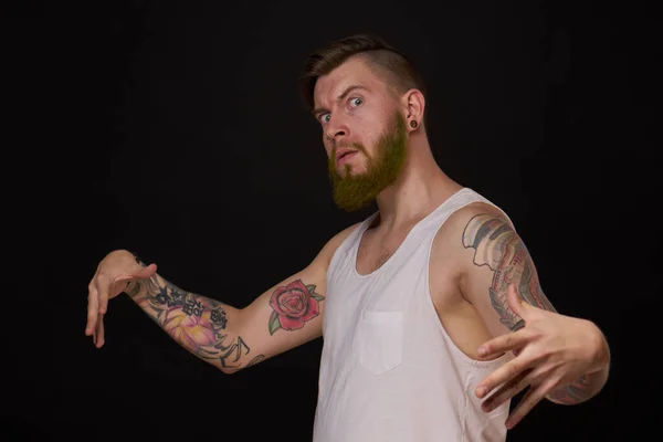 Hombre barbudo con tatuajes en los brazos haciendo gestos con las manos fondo oscuro — Foto de Stock