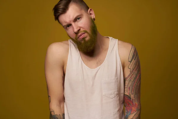 A bearded man with a serious expression in a white t-shirt with tattoos on his arms — Stock Photo, Image