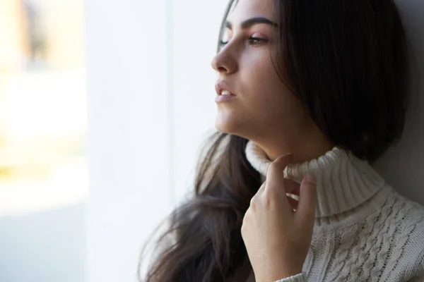 Brunette in a white sweater looks out the window — Stock Photo, Image