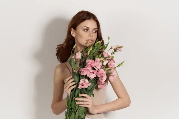 Mooie vrouw in jurk poseren bloemen make-up licht achtergrond — Stockfoto