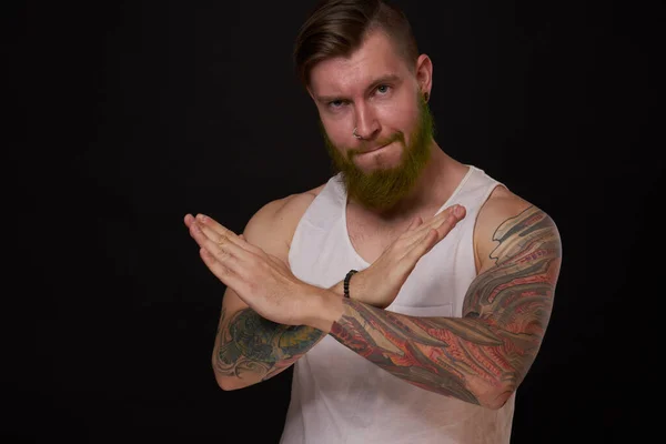 Homme barbu avec des tatouages sur les bras gesticulant avec ses mains fond sombre — Photo