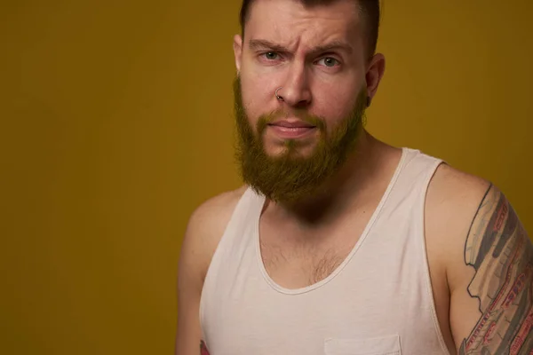 Um homem barbudo com uma expressão séria em uma camiseta branca com tatuagens em seus braços — Fotografia de Stock