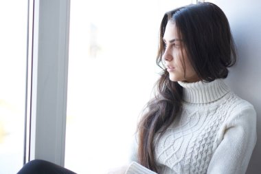 Üzgün kadın pencereden dışarı yakından bakıyor.