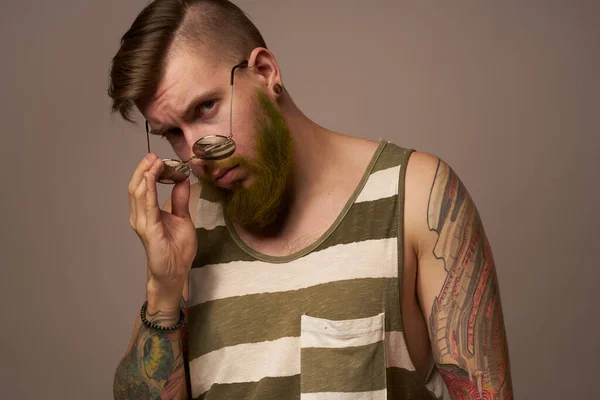 Barbudo hombre en rayas camiseta gafas tatuaje en sus brazos moda — Foto de Stock