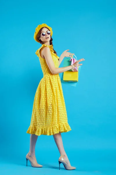 Donna sorridente in un cappello giallo stile shopaholic moda sfondo blu — Foto Stock