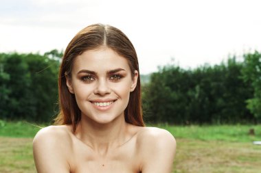 Gülümseyen kadın çekici görünüyor. Çıplak omuzlar. Yeşil yapraklar.