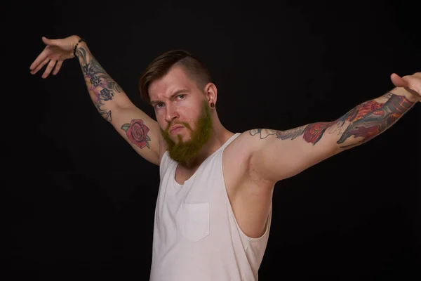 Vousatý muž s tetováním na pažích gestikuluje rukama tmavým pozadím — Stock fotografie