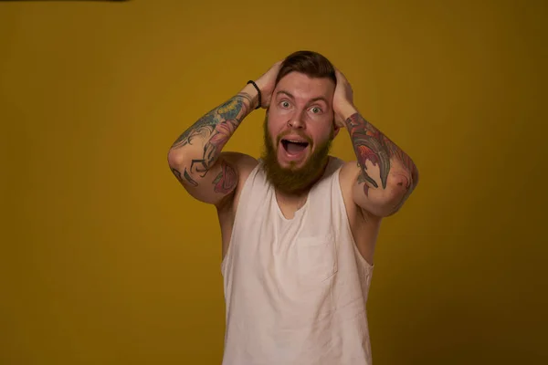 Homme barbu en t-shirt blanc avec des tatouages sur ses bras posant regard sérieux — Photo