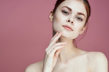 Çıplak omuzlu, çekici, pembe arka planı olan bir kadın.