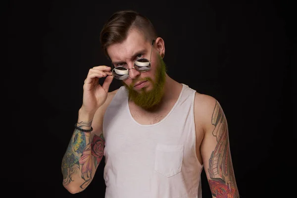 Homem bonito com tatuagens em seus braços moda óculos de sol fundo escuro — Fotografia de Stock