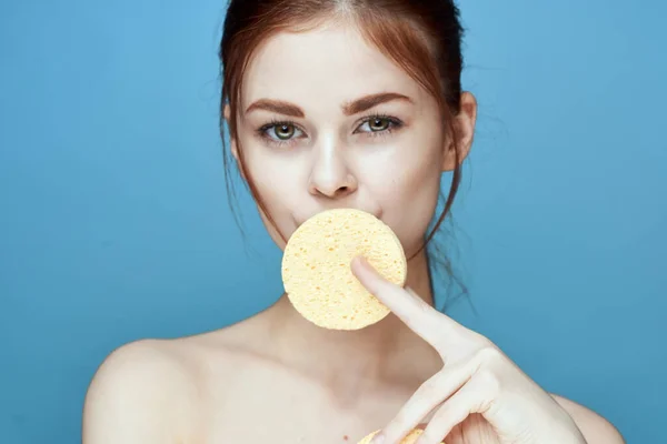 woman with sponges in hands bare shoulders clear skin blue background