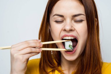 Japon yemek çubuklarıyla suşi yiyen kadın arka planda ışık yayıyor.