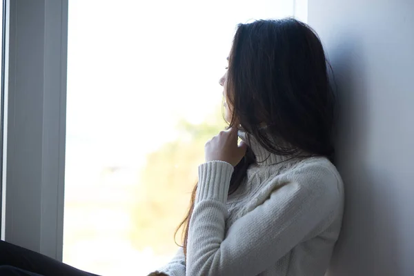 Smutna kobieta przy oknie w białym swetrze samotność — Zdjęcie stockowe
