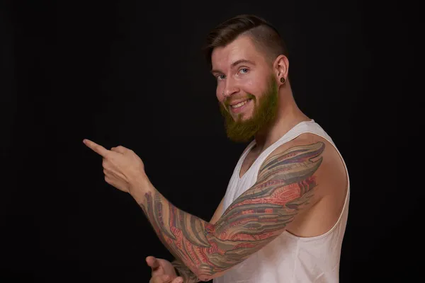 Vousatý muž s tetováním na pažích gestikuluje rukama tmavým pozadím — Stock fotografie