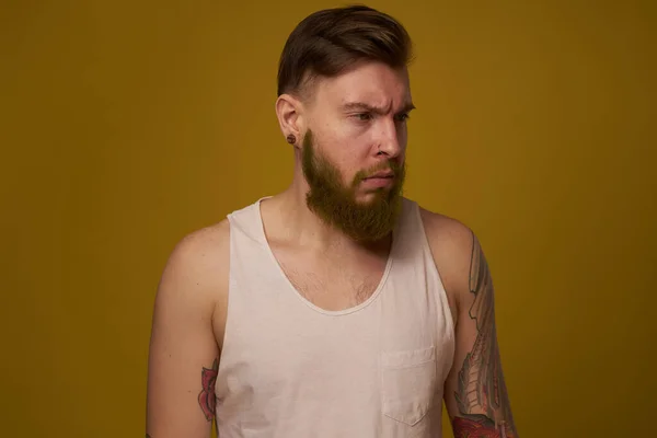 Hombre barbudo en camiseta blanca con tatuajes en sus brazos posando mirada seria — Foto de Stock