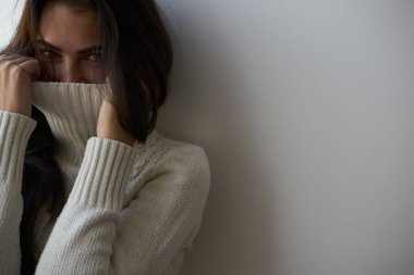 Beyaz kazaklı esmer pencereden dışarı bakıyor.