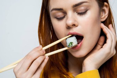 Japon yemek çubuklarıyla suşi yiyen kadın arka planda ışık yayıyor.
