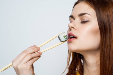 Japon yemek çubuklarıyla suşi yiyen kadın arka planda ışık yayıyor.